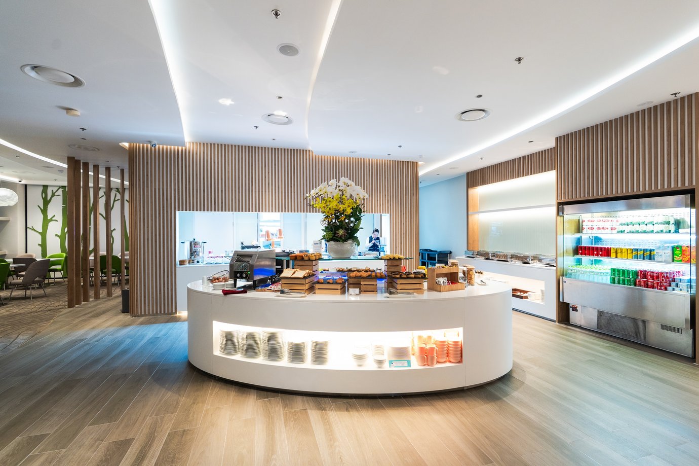 Buffet counter inside Vanda Lounge at Da Nang International Airport Terminal 2, featuring an elegant curved serving island with pastries, refreshments, and orchids under soft ceiling lighting and modern wood-panelled walls.