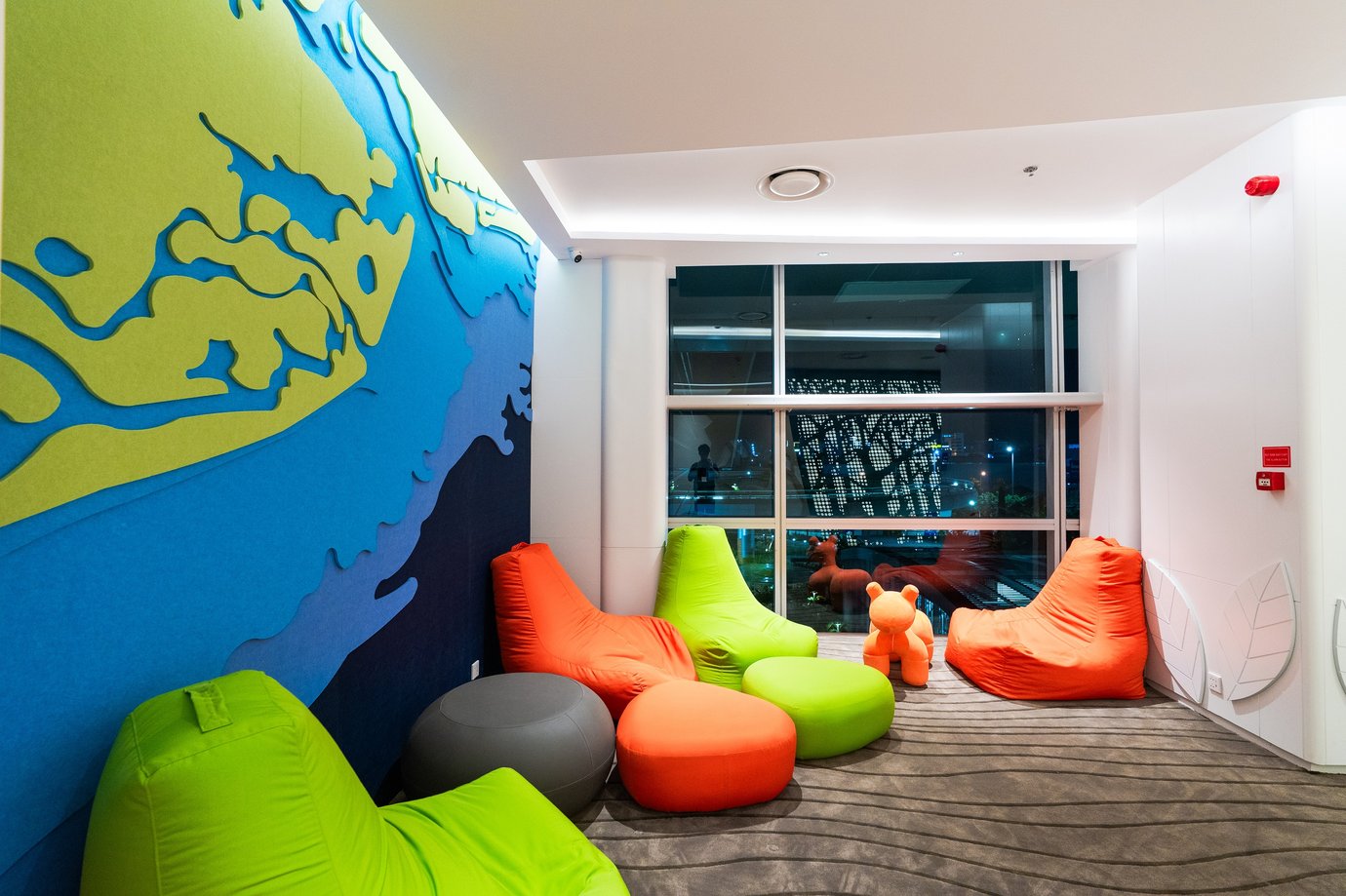 Colorful family space within Vanda Lounge, Da Nang International Airport — bright beanbag seating in green and orange tones, playful wall art, and large windows providing a cheerful environment for young travelers.