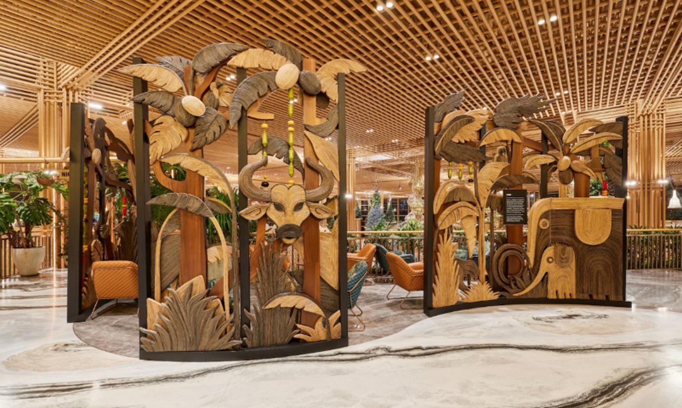 The Kabini Relaxation Lounge at 080 T2 BLR airport, depicting intricate carvings of wildlife, including a bull, an elephant, and tropical foliage. The partitions are part of the airport's lounge decor, creating a natural, earthy ambiance.