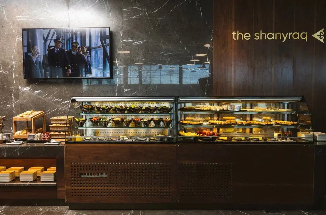 Buffet counter at The Shanyraq Lounge by Air Astana in Almaty International Airport featuring salads, pastries, and fresh fruit.