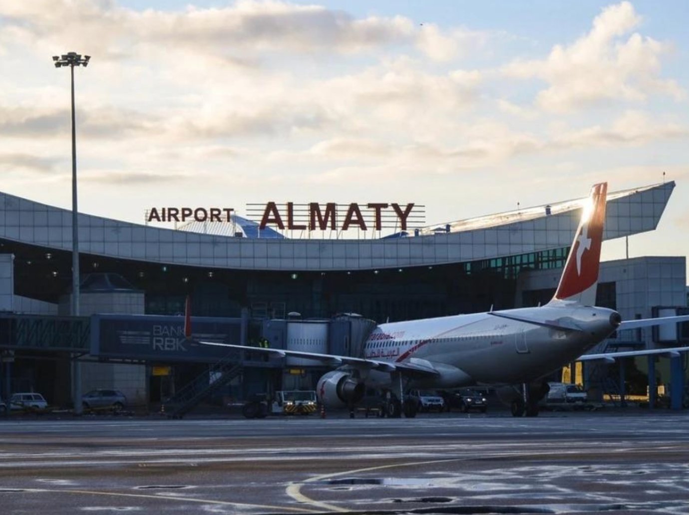Exterior view of Almaty International Airport (ALA) terminal with parked aircraft at sunrise.