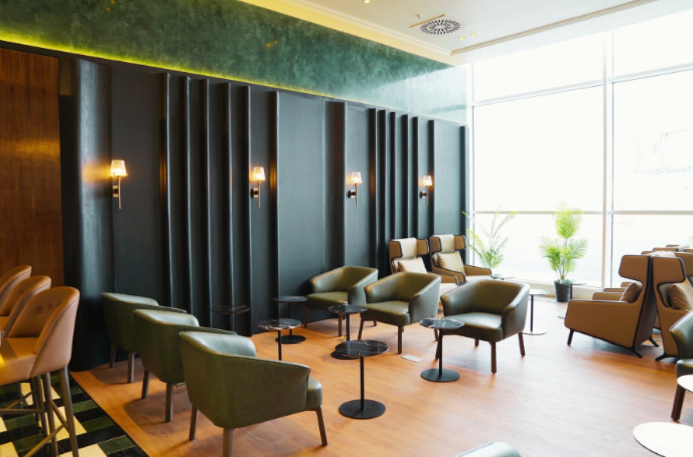 Elegant seating area inside the Extime VIP Arrivals Lounge at Almaty International Airport, featuring soft green armchairs, marble side tables, and warm wall lighting with floor-to-ceiling windows.