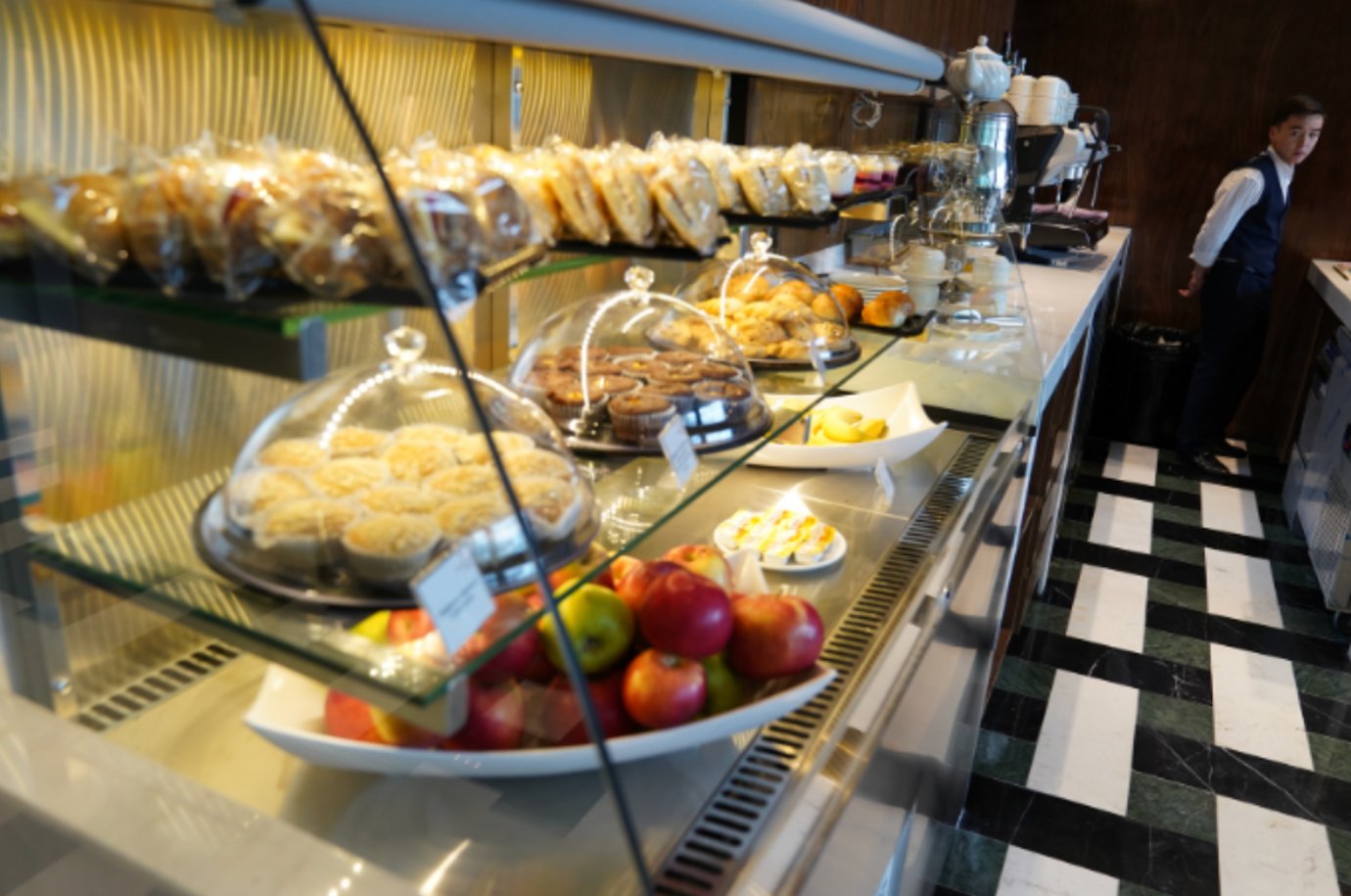 Buffet counter at the Extime VIP Lounge in Almaty International Airport featuring pastries, muffins, fruit, and fresh coffee service.