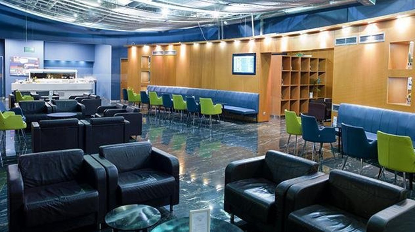 Interior view of the Skyserv Aristotle Onassis Lounge at Athens International Airport, featuring comfortable leather armchairs, modern seating areas with blue and green accents, and a relaxed atmosphere for travellers.