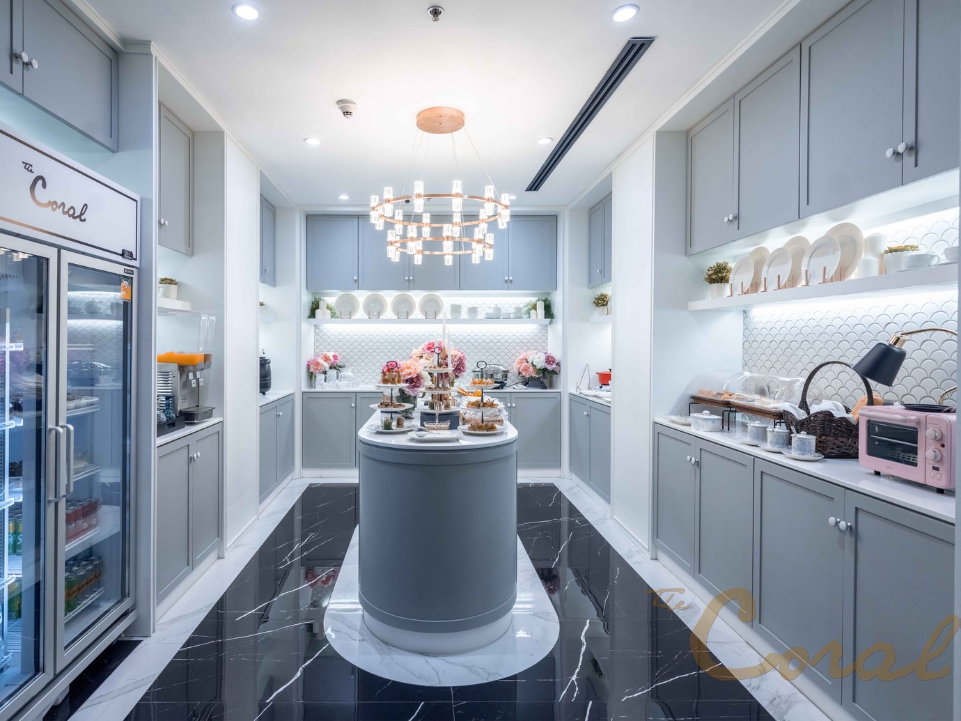 Buffet area at The Coral Finest Business Class Lounge Concourse D Bangkok Suvarnabhumi Airport featuring elegant grey cabinetry, marble flooring, and a central island with pastries, drinks, and desserts.