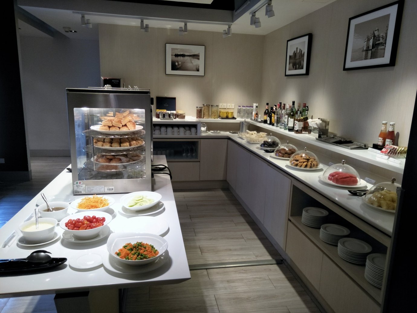 Buffet counter inside the Miracle First Class Lounge, Concourse C, Bangkok Suvarnabhumi Airport, featuring a selection of pastries in a display warmer, bowls of fresh vegetables and salads, assorted fruits, cookies, and beverages.