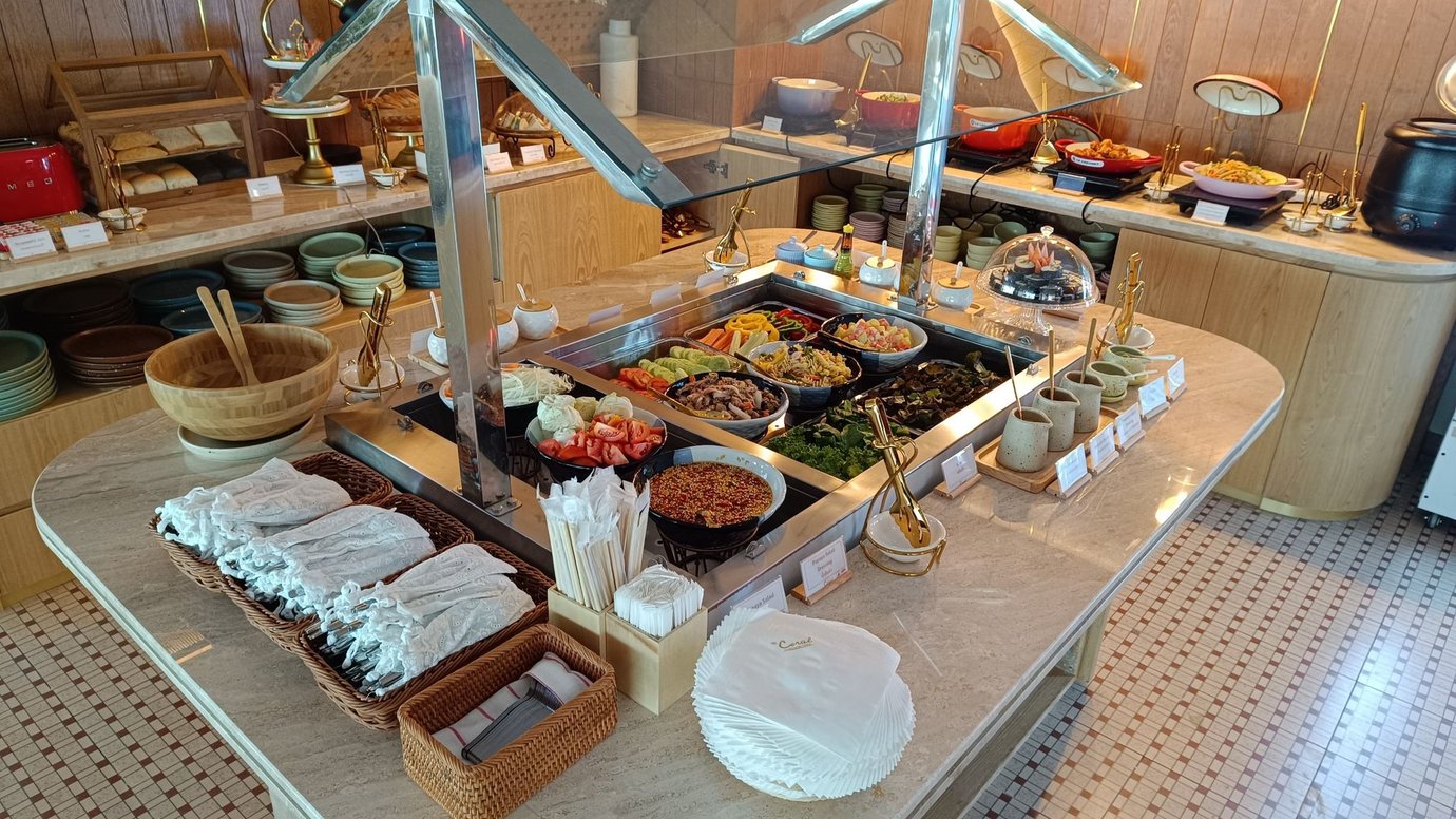 Buffet station at The Coral Finest Business Class Lounge Cocoon, Concourse C Bangkok Suvarnabhumi Airport featuring fresh salads, colorful vegetables, bread, soups, and hot dishes arranged on a marble counter