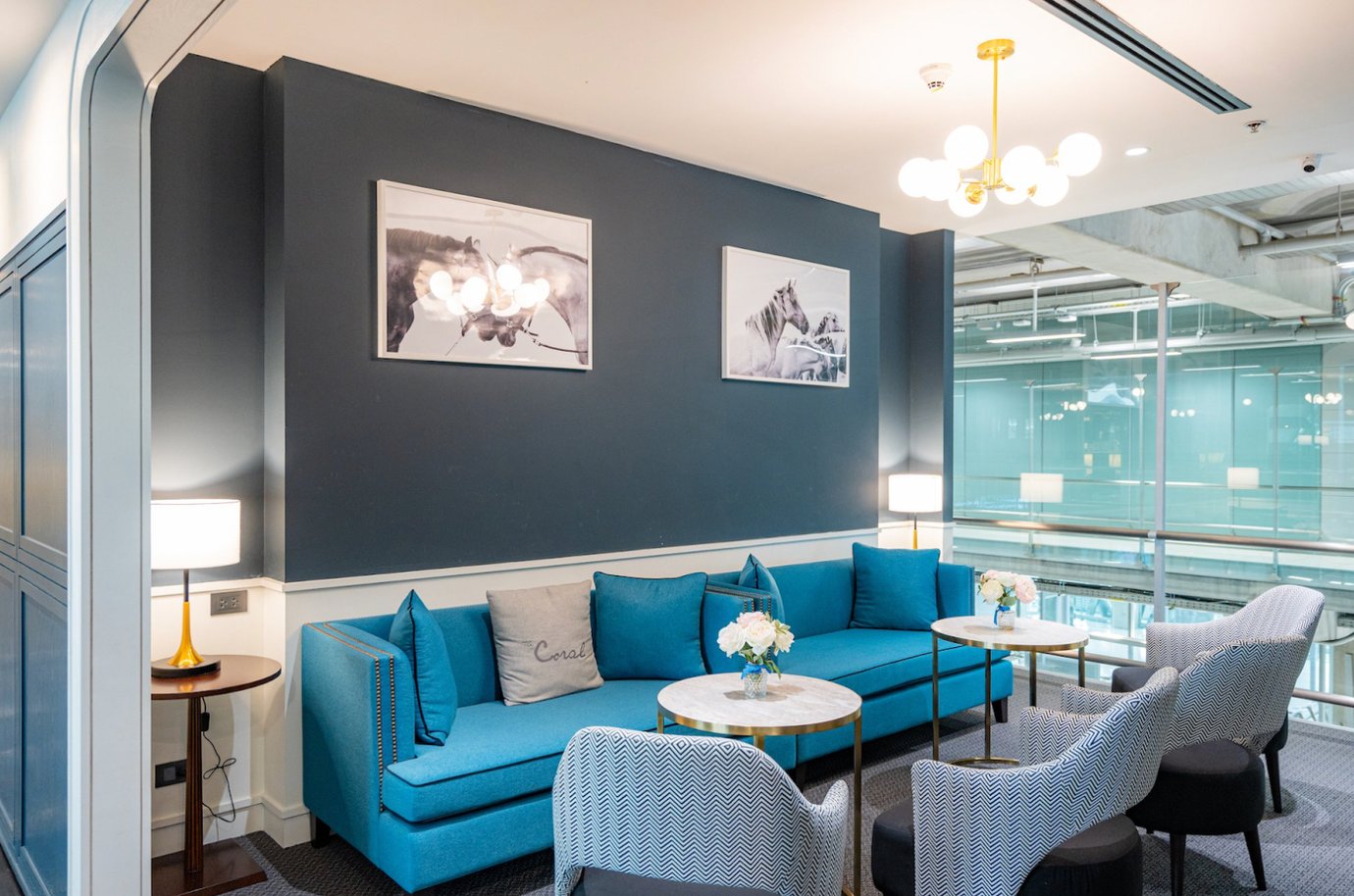 Modern seating area at The Coral Business Class Lounge Concourse D Bangkok Suvarnabhumi Airport with blue sofas, patterned armchairs, marble tables, and elegant lighting.