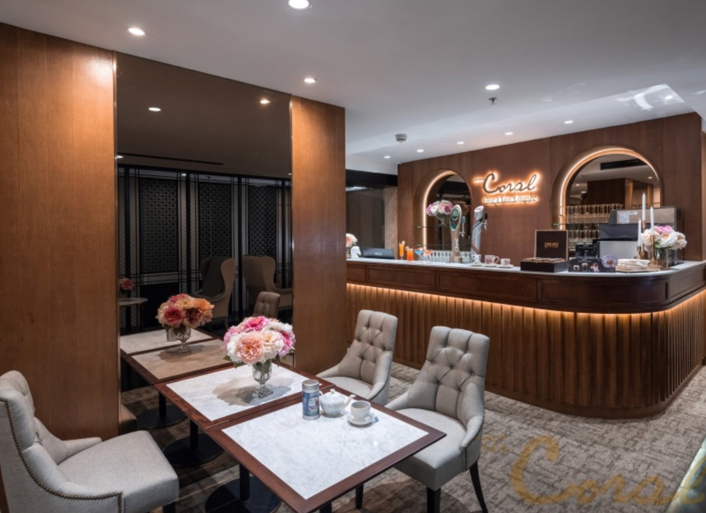 Elegant bar and seating area inside The Coral First Class Lounge Concourse D at Bangkok Suvarnabhumi Airport featuring marble tables, plush chairs, soft lighting, and a stylish wooden bar counter with floral décor.