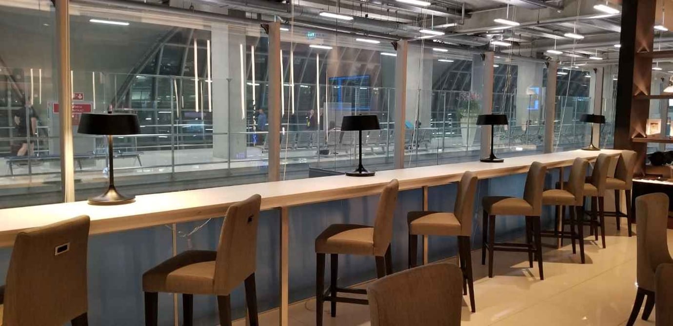 Workstation area at the Miracle First Class Lounge Concourse D Bangkok Suvarnabhumi Airport featuring a high-top counter with power outlets, elegant task lamps, and runway-view windows ideal for business travellers.