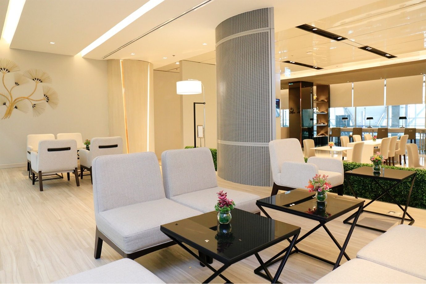 Seating area inside the Miracle Business Class Lounge Concourse D at Bangkok Suvarnabhumi Airport featuring modern beige armchairs, black coffee tables with small flower arrangements, and a bright elegant interior.