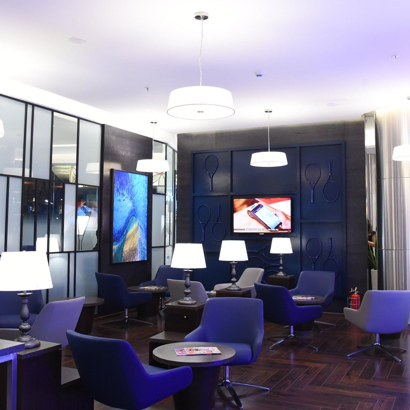 Modern seating area at the Centurion Lounge Mumbai Airport T2 showcasing blue and grey chairs, warm lighting, and contemporary wall décor. Modern seating area at the Centurion Lounge Mumbai Airport T2 showcasing blue and grey chairs, warm lighting, and contemporary wall décor.