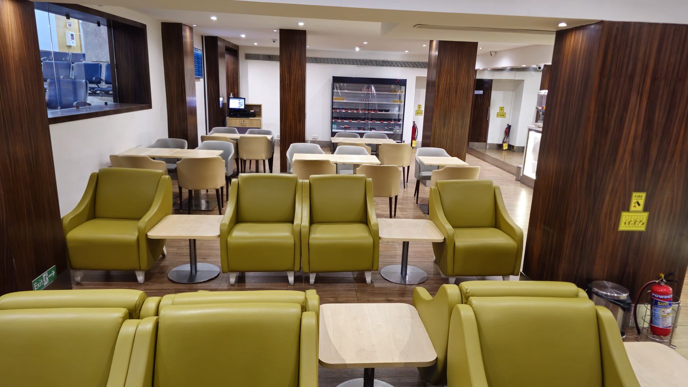Good Times Bar lounge seating area at Mumbai Airport T1 with yellow armchairs, dining tables, and wood-panelled walls. Good Times Bar lounge seating area at Mumbai Airport T1 with yellow armchairs, dining tables, and wood-panelled walls.