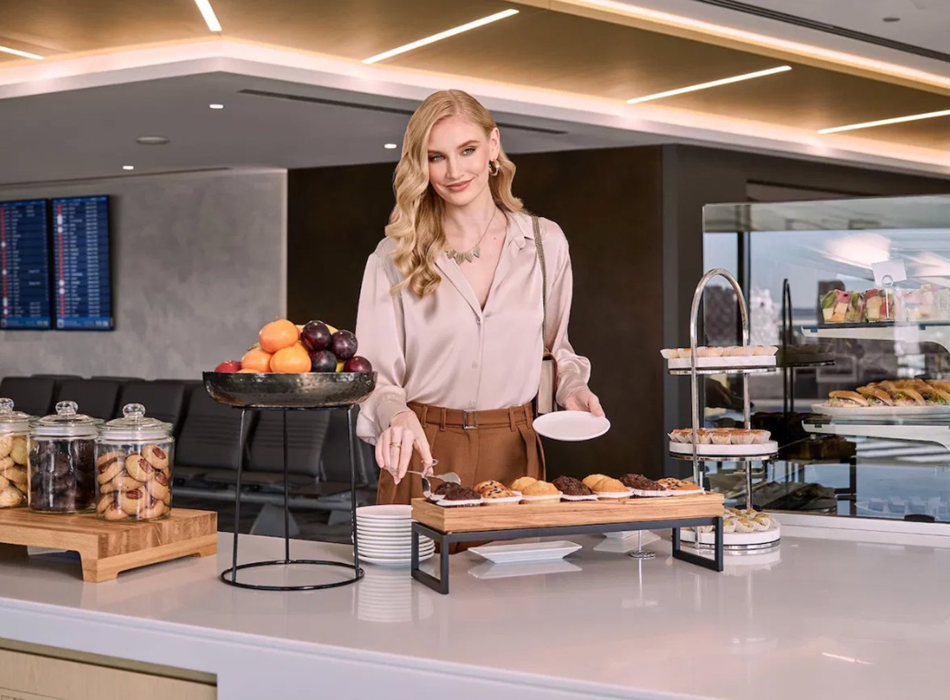 Passenger enjoying the buffet selection at Flydubai Business Lounge in Dubai Airport Terminal 2, featuring pastries, cookies, fresh fruit, and a modern, well-lit interior with elegant lounge design.