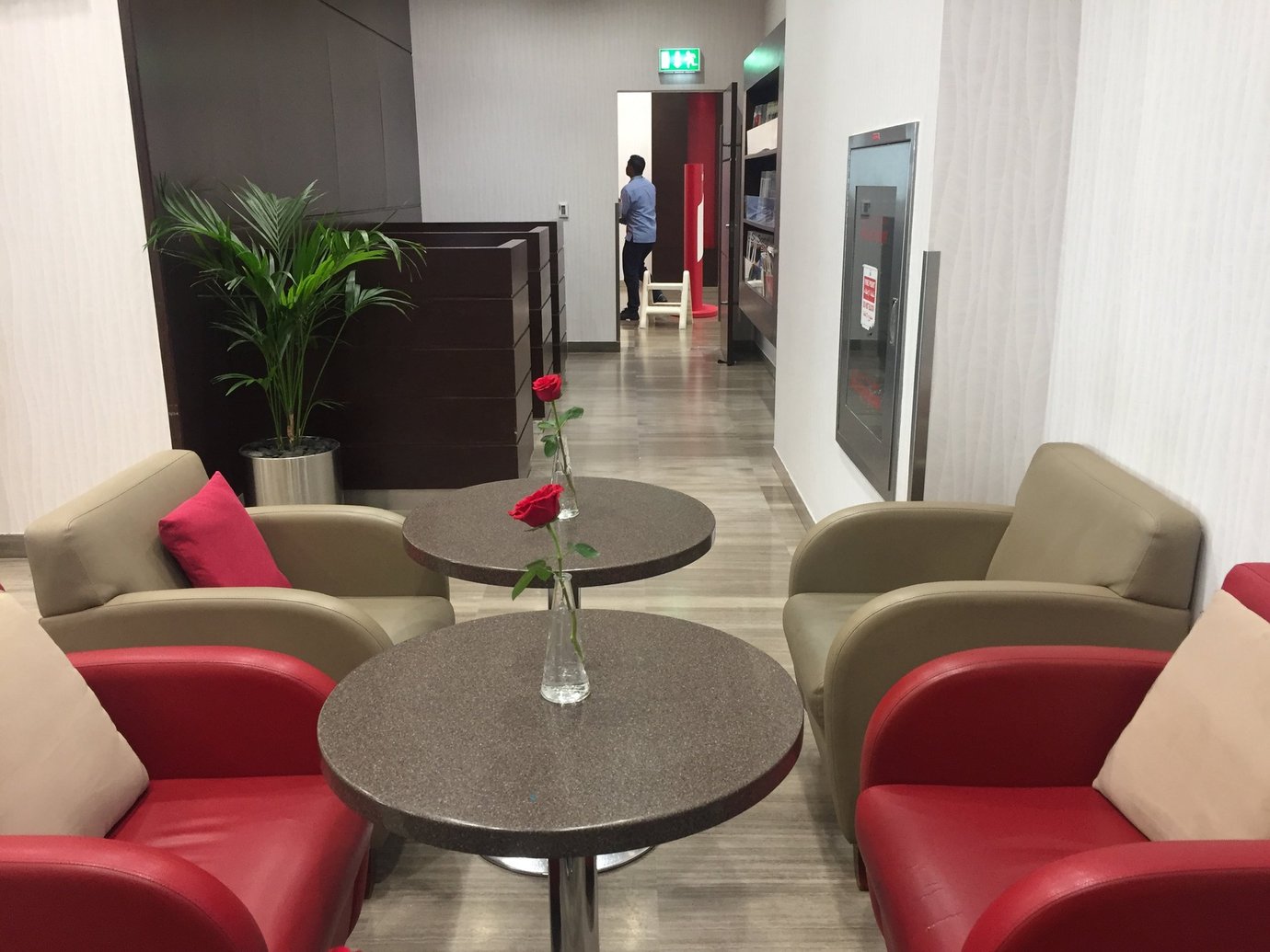 Modern seating area inside Marhaba Lounge at Dubai Airport Terminal 2, featuring red and beige armchairs, small round tables with single red roses, soft lighting, and a calm atmosphere near the reading corner.