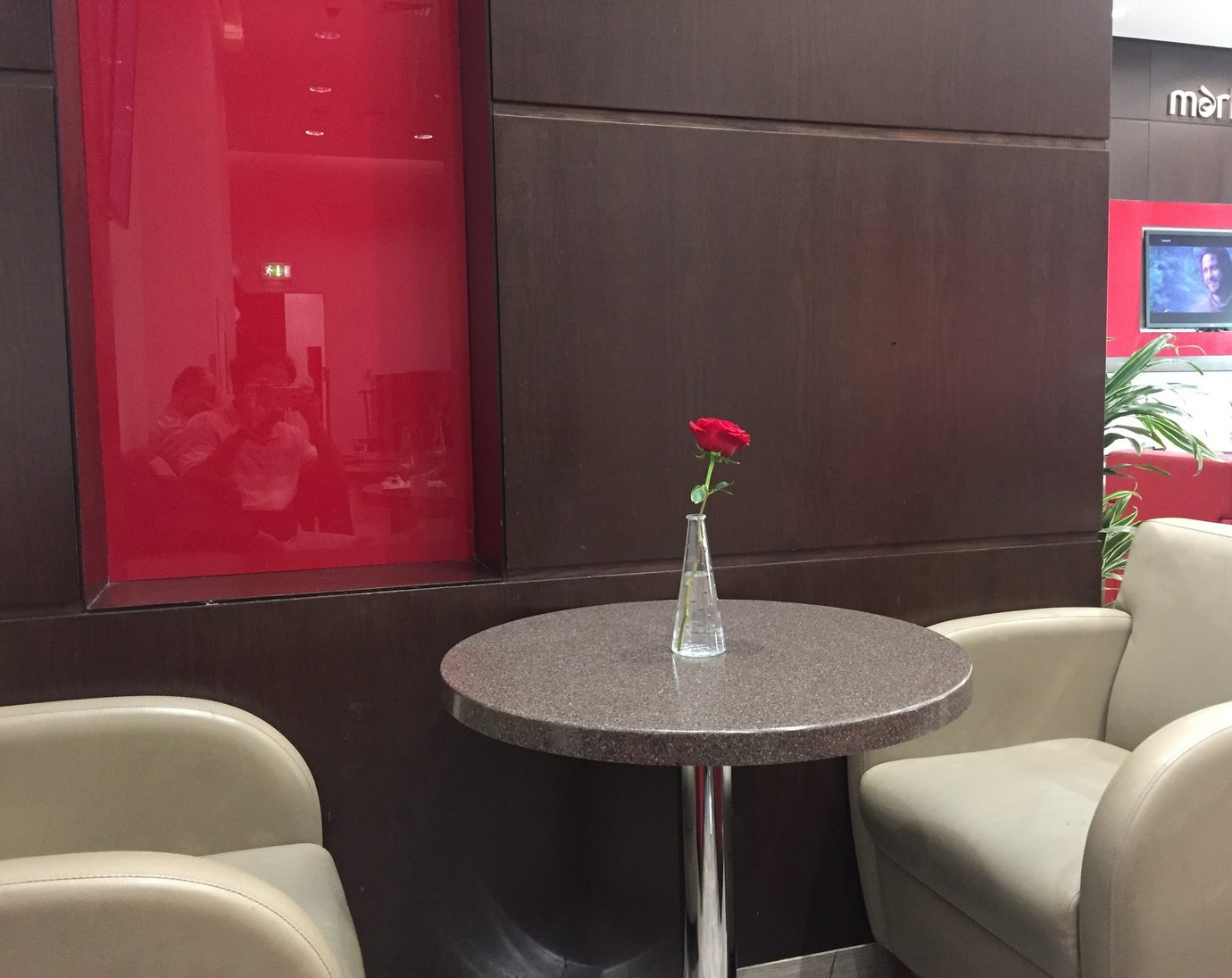 Marhaba Lounge Dubai Terminal 2 seating area with beige armchairs and a table decorated with a red rose, set against dark wood and red accents for a calm, stylish look.