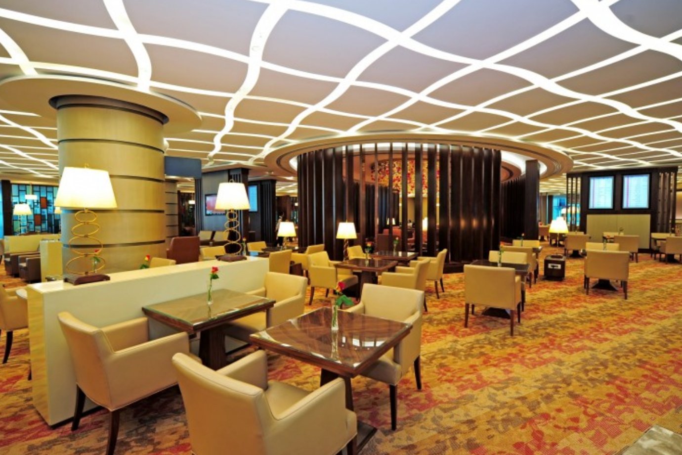 Elegant seating area inside the Emirates First Class Lounge in Concourse A, Dubai International Airport. The space features beige leather armchairs arranged around glossy wooden tables, with warm ambient lighting from spiral gold lamps. Elegant seating area inside the Emirates First Class Lounge in Concourse A, Dubai International Airport. The space features beige leather armchairs arranged around glossy wooden tables, with warm ambient lighting from spiral gold lamps.