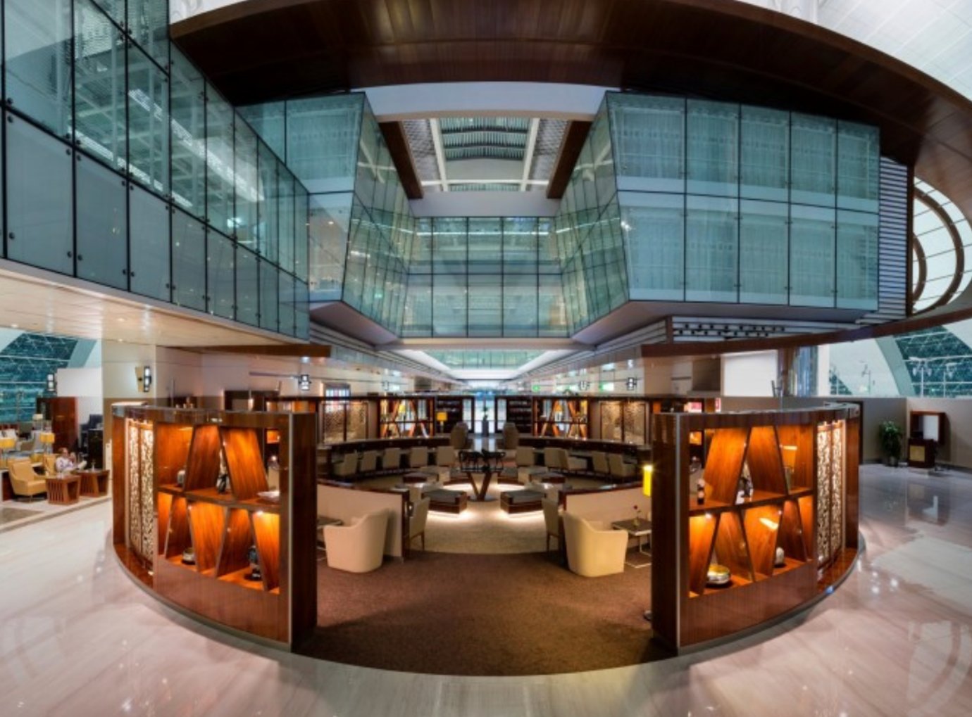 Spacious Emirates Business Class Lounge in Concourse A at Dubai International Airport Terminal 3, featuring elegant wood-panelled partitions, curved seating areas, warm ambient lighting, and a high glass atrium ceiling overlooking the concourse. Spacious Emirates Business Class Lounge in Concourse A at Dubai International Airport Terminal 3, featuring elegant wood-panelled partitions, curved seating areas, warm ambient lighting, and a high glass atrium ceiling overlooking the concourse.