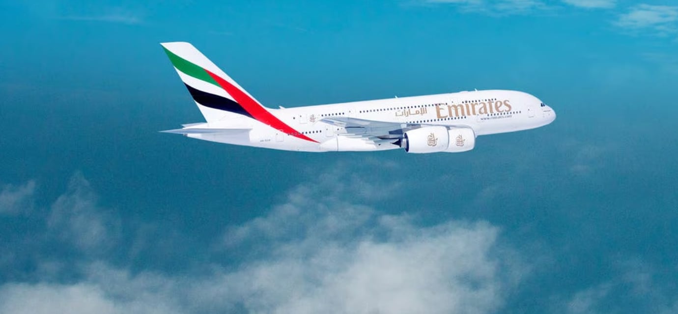 Emirates Airbus A380 flying above the clouds with bright blue sky background, showcasing the airline’s signature red, green, black, and white tail design. Emirates Airbus A380 flying above the clouds with bright blue sky background, showcasing the airline’s signature red, green, black, and white tail design.