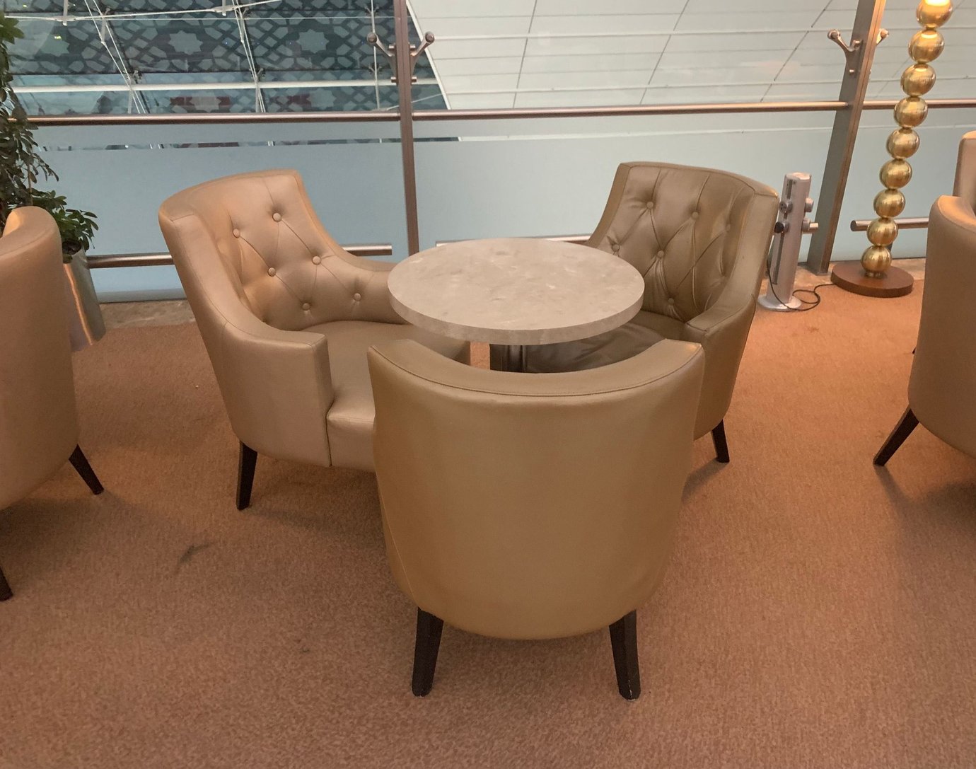 Small seating arrangement inside the Marhaba Lounge at Dubai International Airport Terminal 3 Concourse A, featuring beige leather armchairs around a marble table in a cozy, carpeted area overlooking the terminal. Small seating arrangement inside the Marhaba Lounge at Dubai International Airport Terminal 3 Concourse A, featuring beige leather armchairs around a marble table in a cozy, carpeted area overlooking the terminal.