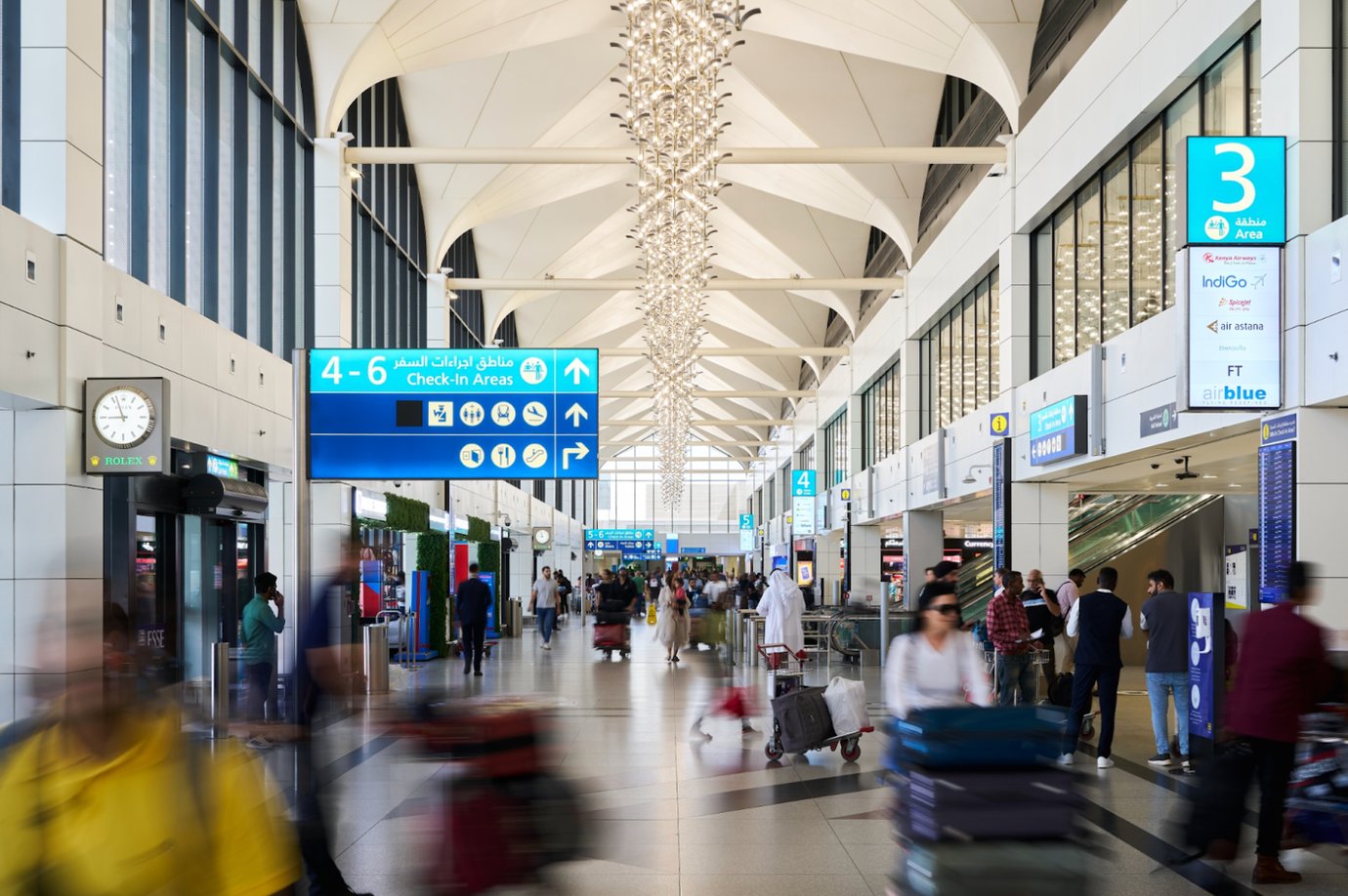 Busy check-in area at Dubai International Airport Terminal 1 featuring bright natural light, modern ceiling architecture, large directional signage, and passengers moving with luggage carts. Busy check-in area at Dubai International Airport Terminal 1 featuring bright natural light, modern ceiling architecture, large directional signage, and passengers moving with luggage carts.