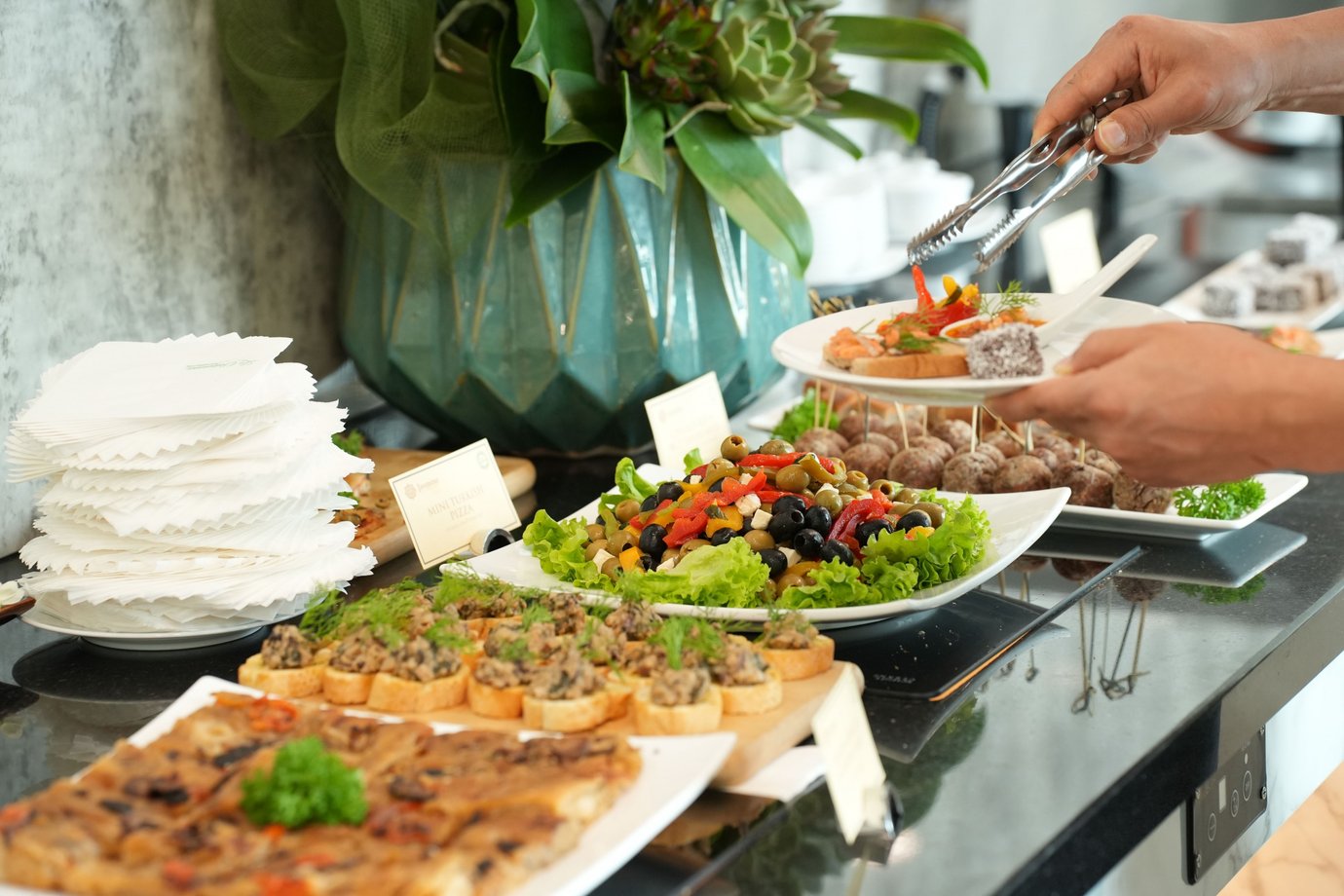 Buffet at the Jasmine Halal Lounge, featuring assorted cold appetizers, canapés, olives, and salads being served from a marble counter with floral décor. Buffet at the Jasmine Halal Lounge, featuring assorted cold appetizers, canapés, olives, and salads being served from a marble counter with floral décor.