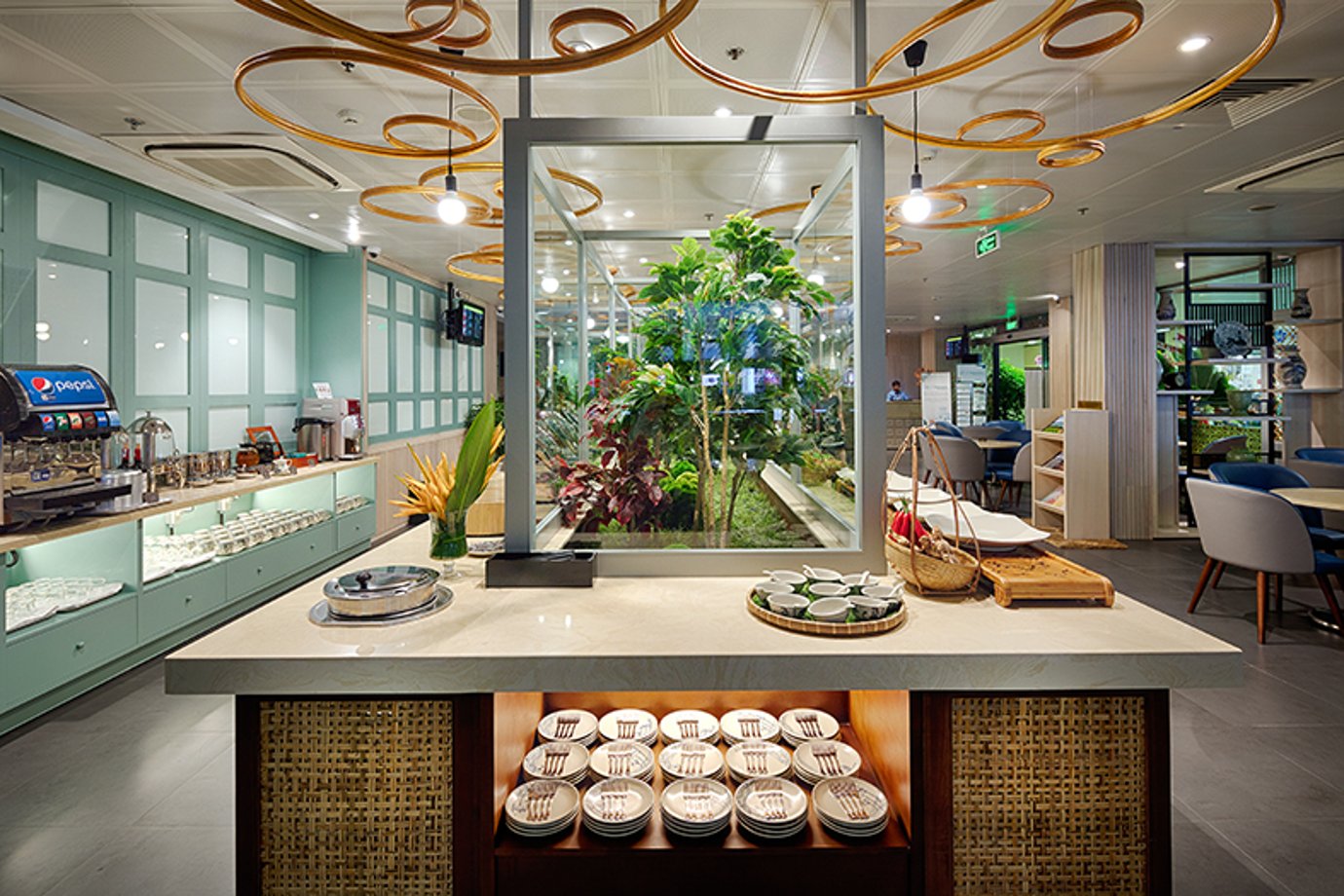 Buffet island at Le Saigonnais Business Lounge with white bowls, a glass-enclosed indoor garden, mint-green walls, and gold loop pendant lights. Buffet island at Le Saigonnais Business Lounge with white bowls, a glass-enclosed indoor garden, mint-green walls, and gold loop pendant lights.