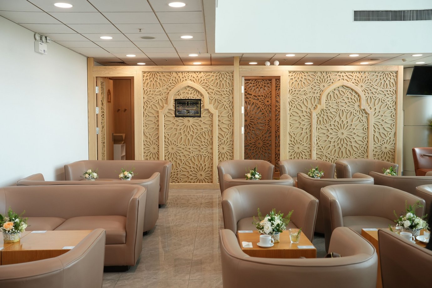 Jasmine Halal Lounge prayer area with carved wooden mihrab panels and beige seating. Jasmine Halal Lounge prayer area with carved wooden mihrab panels and beige seating.