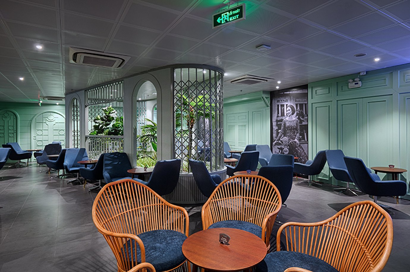 Seating area inside Le Saigonnais Business Lounge at Ho Chi Minh City Tan Son Nhat Airport, featuring mint-green walls, rattan chairs, blue armchairs, indoor plants, and soft ambient lighting. Seating area inside Le Saigonnais Business Lounge at Ho Chi Minh City Tan Son Nhat Airport, featuring mint-green walls, rattan chairs, blue armchairs, indoor plants, and soft ambient lighting.