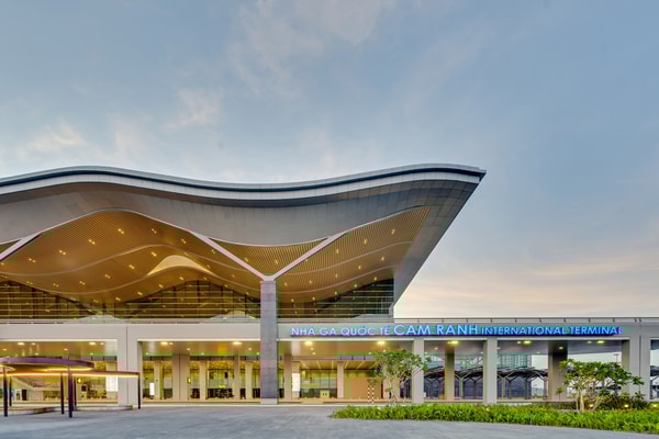 Exterior view of Cam Ranh International Airport terminal in Vietnam with modern wave-shaped roof design at sunset.