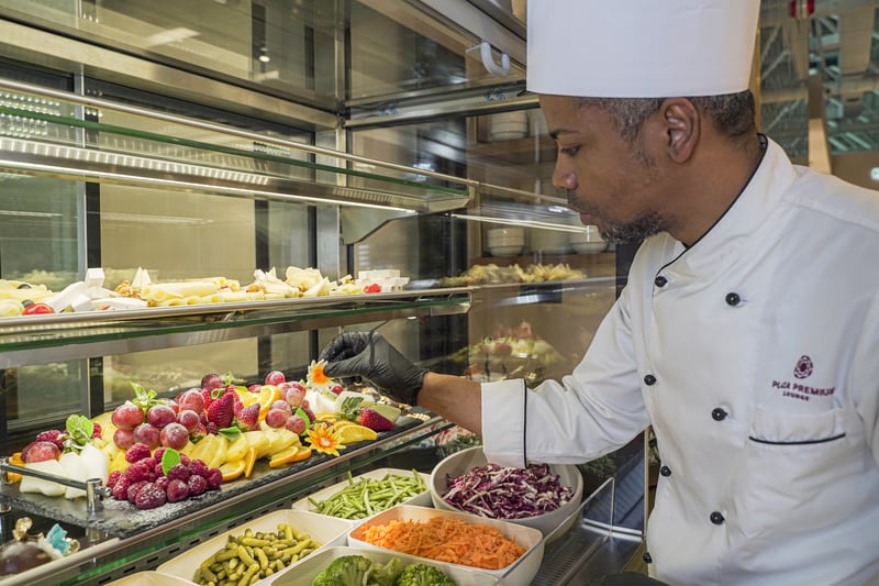 A chef at Plaza Premium Lounge, Leonardo da Vinci-Fiumicino Airport, arranges fresh fruit and vegetable displays in a self-serve food area.