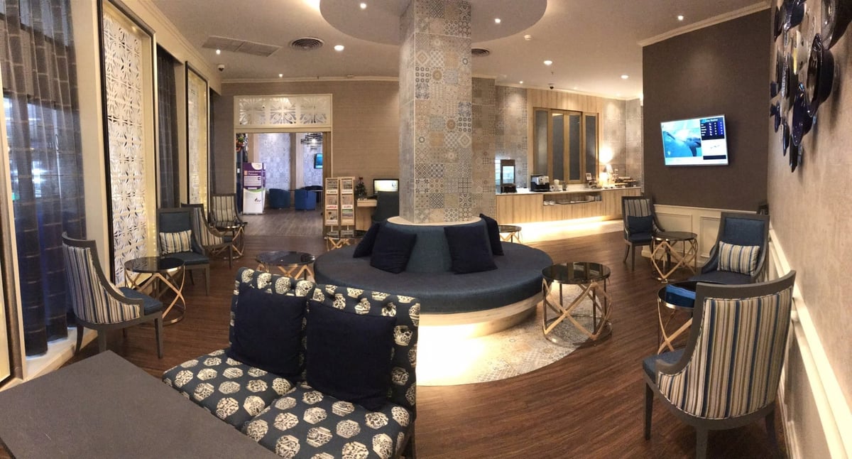 Interior of the blue ribbon lounge at CNX airport featuring plush armchairs, a central circular seating area with navy cushions, and a sleek service counter in the background.