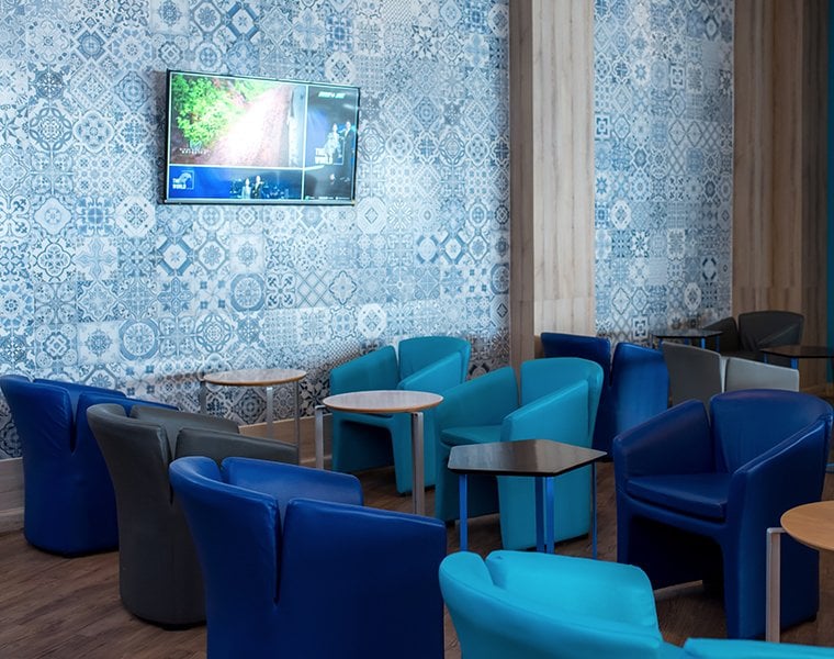 Colourful seating area inside the Bangkok Airways Boutique Lounge at Chiang Mai International Airport (CNX), featuring modern blue and grey armchairs, round and geometric tables, and a patterned blue tile accent wall.