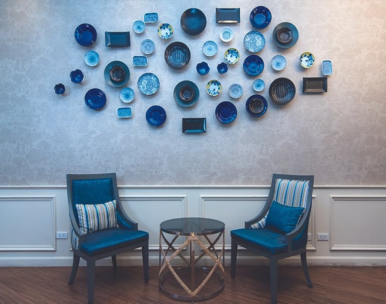 Elegant seating area at the Blue Ribbon Club Lounge in Chiang Mai International Airport (CNX), featuring two blue upholstered chairs with striped cushions, a round glass-top table, and a decorative wall installation.