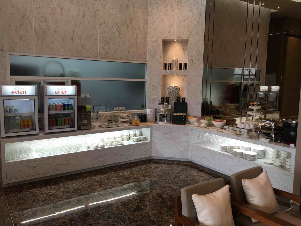 Buffet station at The Coral Executive Lounge in Chiang Mai International Airport (CNX) International Terminal, featuring marble counters, Evian beverage coolers, a coffee machine, salad bowls, pastries, and a selection of glassware and tableware.