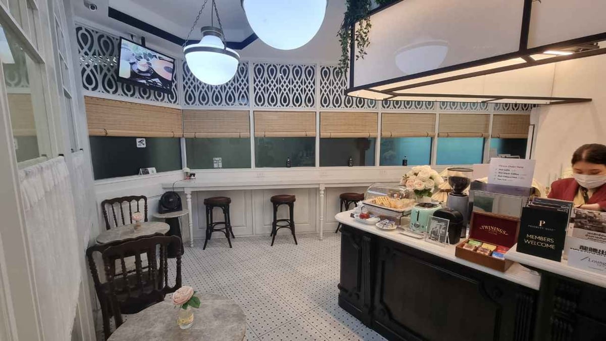 Interior of The Coral Executive Lounge at Chiang Mai Airport (CNX) domestic terminal, featuring classic-style seating, a bar counter with snacks and tea, and a staff member behind the counter.