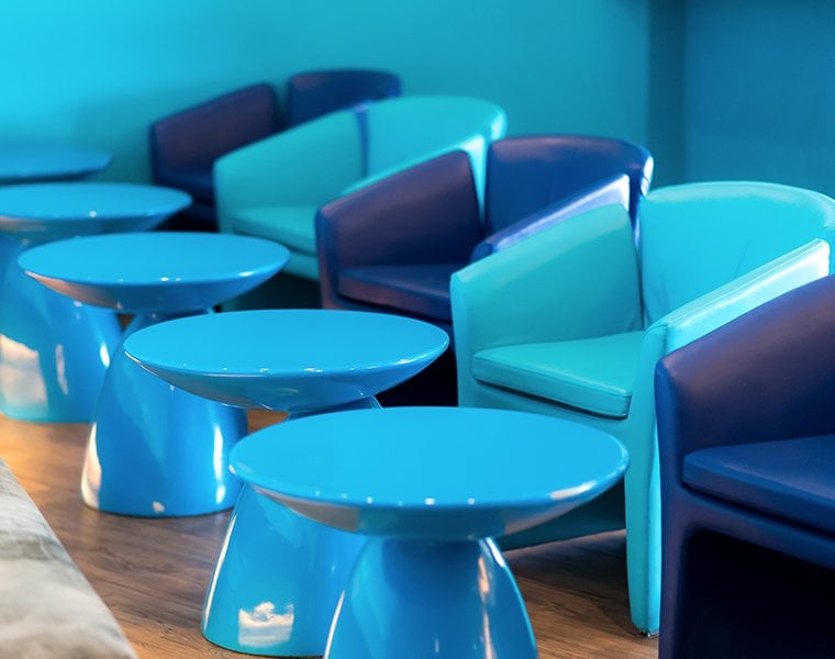 Modern lounge seating at Bangkok Airways Boutique Lounge in Chiang Mai International Airport (CNX), showcasing vibrant turquoise and navy armchairs paired with glossy blue sculptural tables on wood flooring against a matching blue wall.