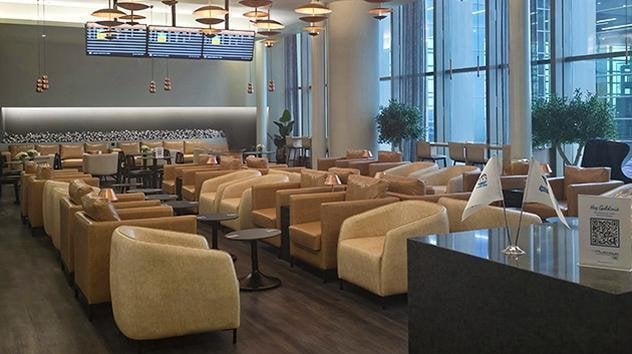 Elegant seating area at Çelebi Platinum International Lounge, Çukurova International Airport, featuring plush armchairs, flight status monitors, floor-to-ceiling windows, and modern ambient lighting.
