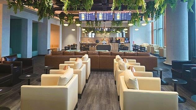 Spacious seating area at Çelebi Platinum Domestic Lounge, Çukurova International Airport, featuring modern armchairs, flight information screens, lush ceiling greenery, and a view toward the buffet and bar.