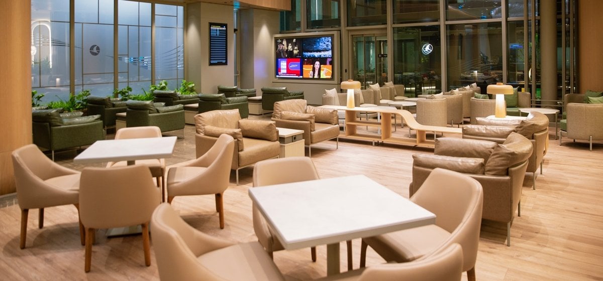 Modern interior of the Turkish Airlines CIP Lounge at Çukurova International Airport, featuring leather armchairs, marble-top dining tables, large windows, flat-screen TVs, and ambient lighting in a spacious, family-friendly setting.