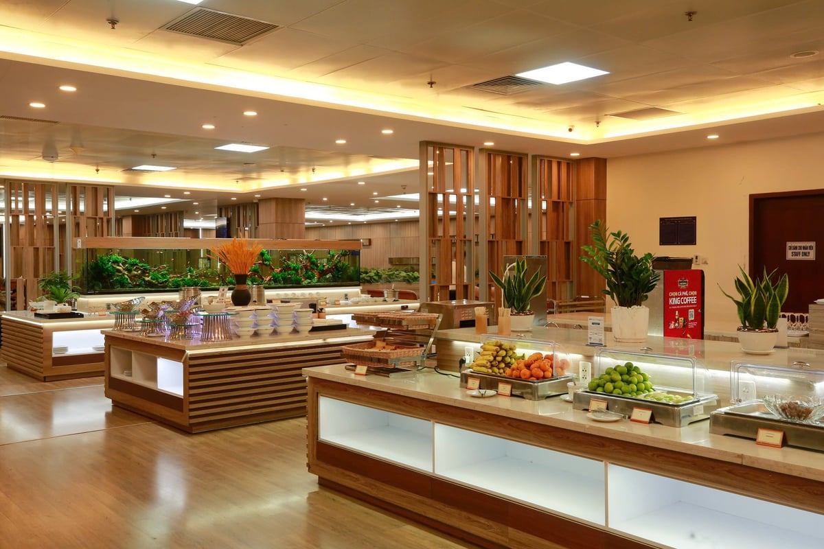 Buffet area at Vietnam Airlines Lotus Lounge in Da Nang Airport showcasing fresh fruit, plated snacks, modern food stations, and a large built-in aquarium in a spacious, well-lit setting with wood accents.
