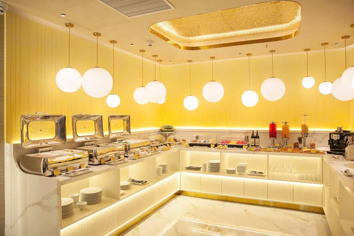 Buffet area inside Nam A Bank Premier Lounge at Da Nang Airport featuring hanging globe lights, marble countertops, hot and cold food stations, drink dispensers, and elegant gold-accented design.
