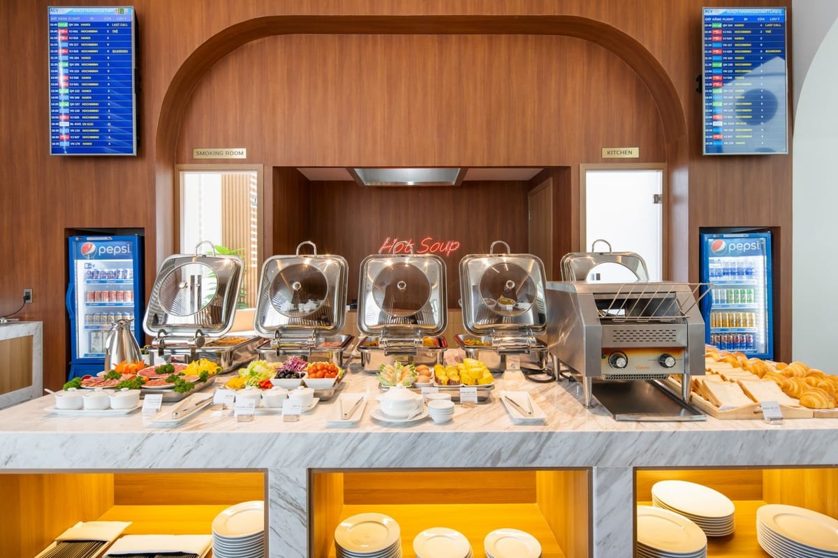 Buffet spread at the Vietcombank Priority Lounge in Da Nang Airport, showcasing a variety of hot dishes, salad options, croissants, eggs, and fresh fruits, with a sleek marble counter, dual beverage coolers, and neon “Hot Soup” signage