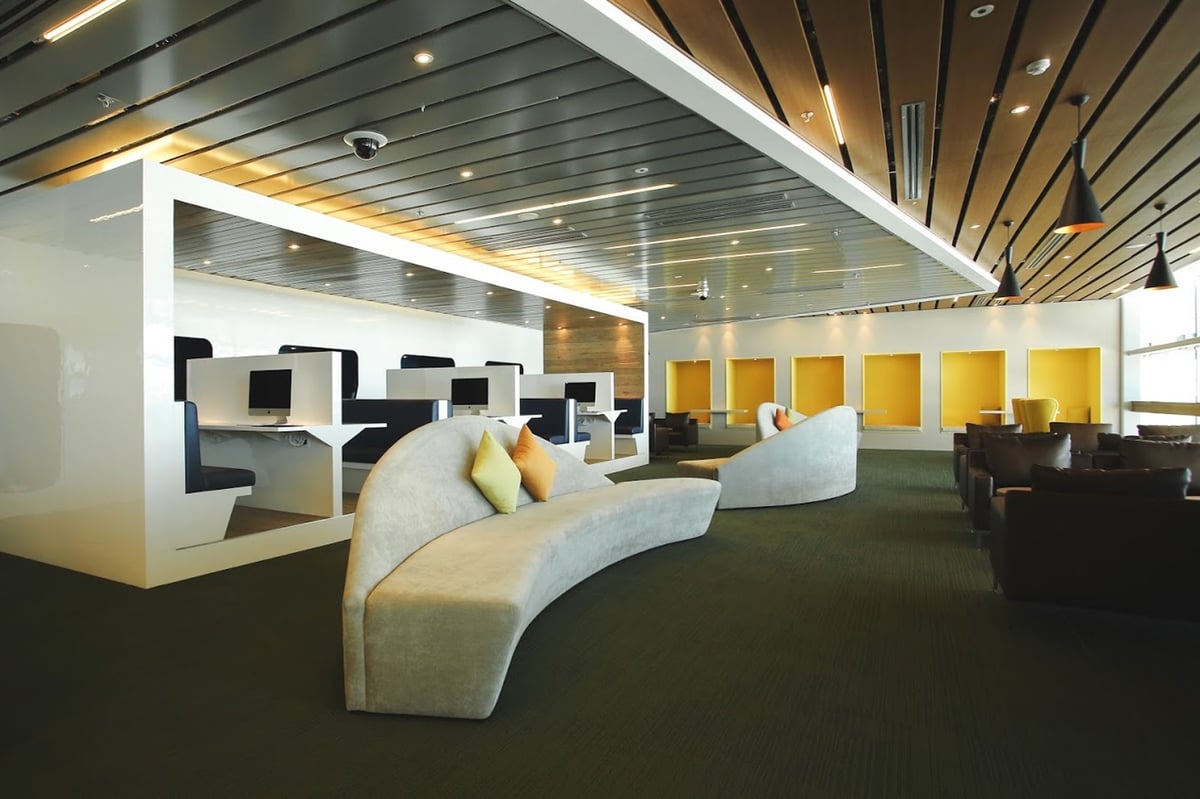 Modern workstation and seating area at CIP Orchid Lounge 1, Da Nang Airport Terminal 2, featuring iMac desks, yellow productivity booths, and curved grey sofas for business travellers