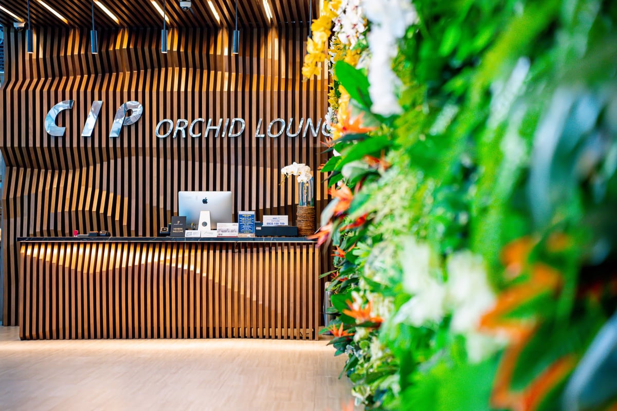 Entrance to CIP Orchid Lounge at Da Nang Airport Terminal 2 featuring a modern wooden slat reception desk, iMac check-in counter, and a lush vertical garden wall with tropical flowers.