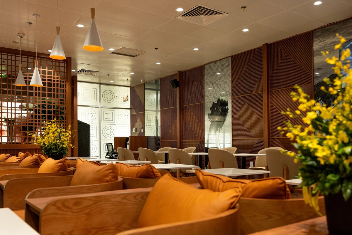 Stylish seating area inside SH Premium Lounge at Da Nang International Airport featuring modern wooden decor, warm lighting, cushioned armchairs, and decorative yellow flowers for a relaxing pre-flight atmosphere.