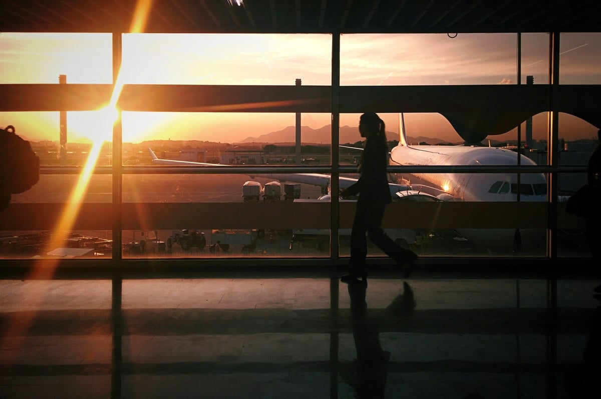 Silhouette of a traveler walking past large terminal windows at Da Nang International Airport, with a plane parked on the tarmac and a warm sunset casting golden light across the scene.