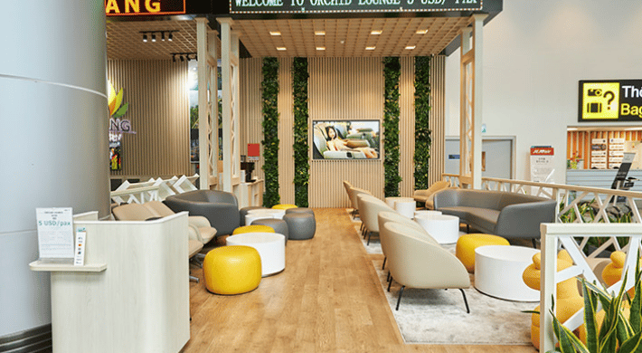 Modern seating at CIP Orchid Lounge 3 in Da Nang Airport’s arrivals area, featuring soft armchairs, ottomans, and greenery near baggage claim for passenger relaxation.