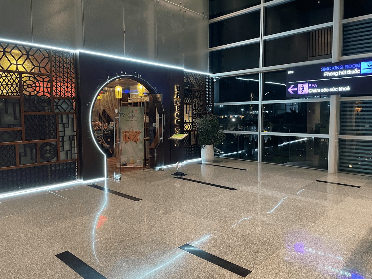 Entrance to Bamboo Spa at Da Nang International Airport, featuring a circular, neon-lit doorway, traditional wooden lattice paneling, and warm interior lighting, with a nearby sign directing to the smoking room and health spa facilities.