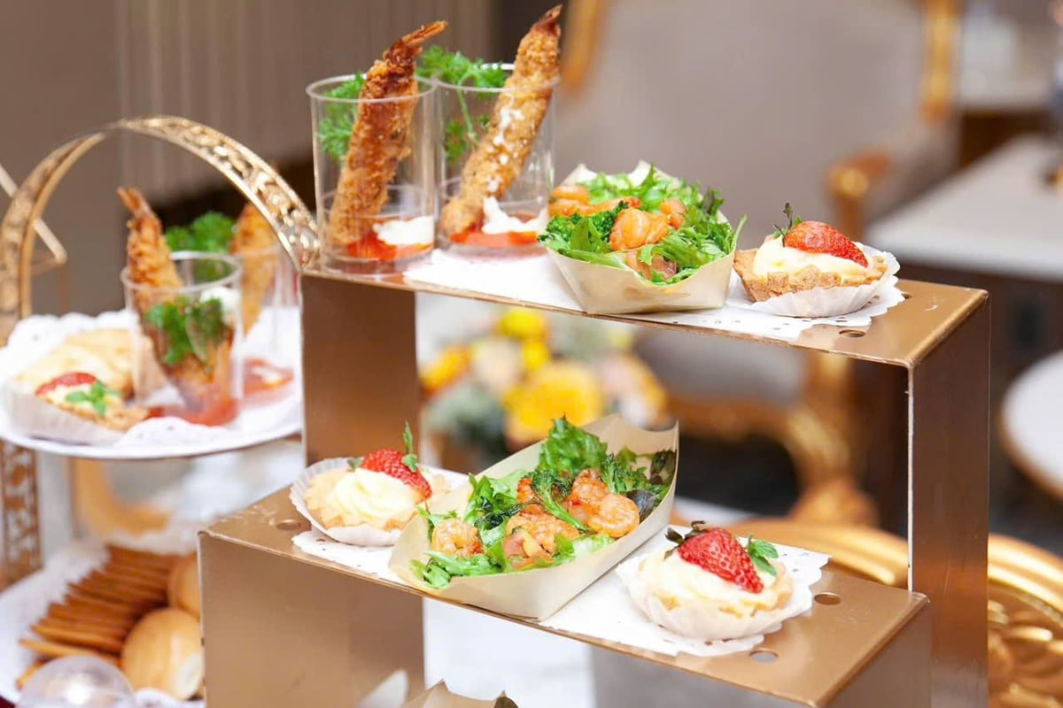 Close-up of elegant canapé and dessert selection at Nam A Bank Premier Lounge in Da Nang Airport, featuring shrimp salad cups, fried prawn skewers, and strawberry-topped cream tarts on a gold-tiered stand.